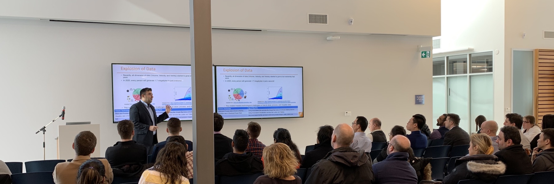 Amir Tavasoli presenting his "My Journey as a Data Scientist" talk to an audience at Lakehead University, with "Explosion of Data" slides on screen